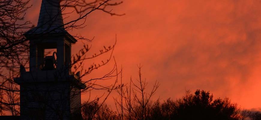 Kerktoren met oranje lucht bij zonsopkomst
